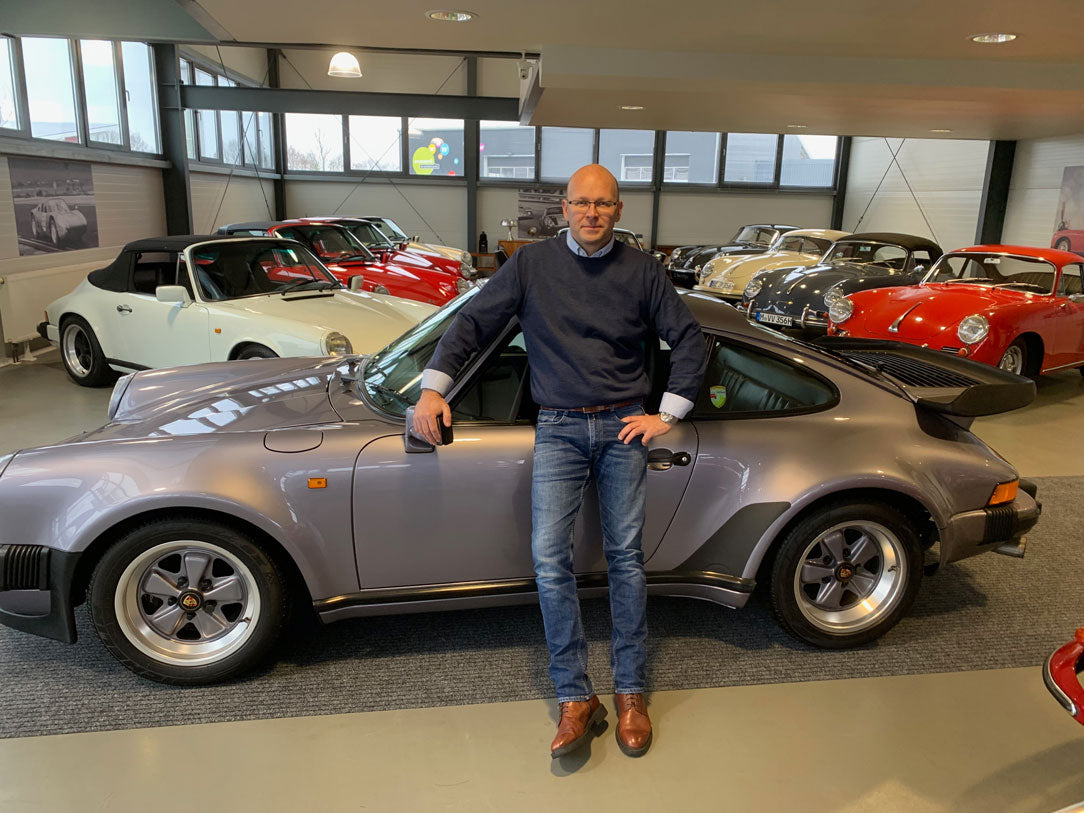 Dennis Nachtigal lehnt an einem klassischem Porsche Sportwagen in seiner Fahrzeughalle